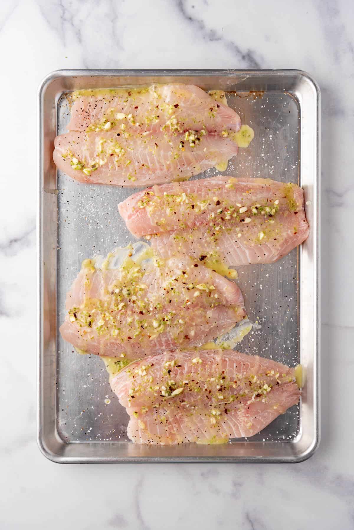 An overhead image of tilapia filets on a baking sheet with lime juice, zest, and garlic on top.