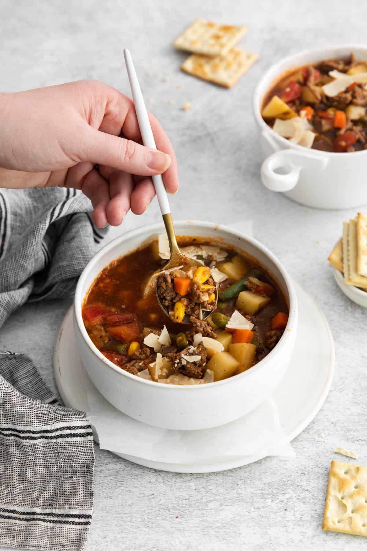 A hand holding a spoon scooping up some vegetable beef soup.