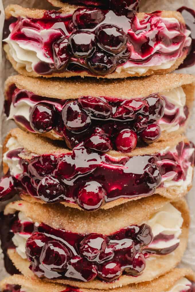 A close image of juice blueberry pie filling on top of dessert tacos with cheesecake filling.