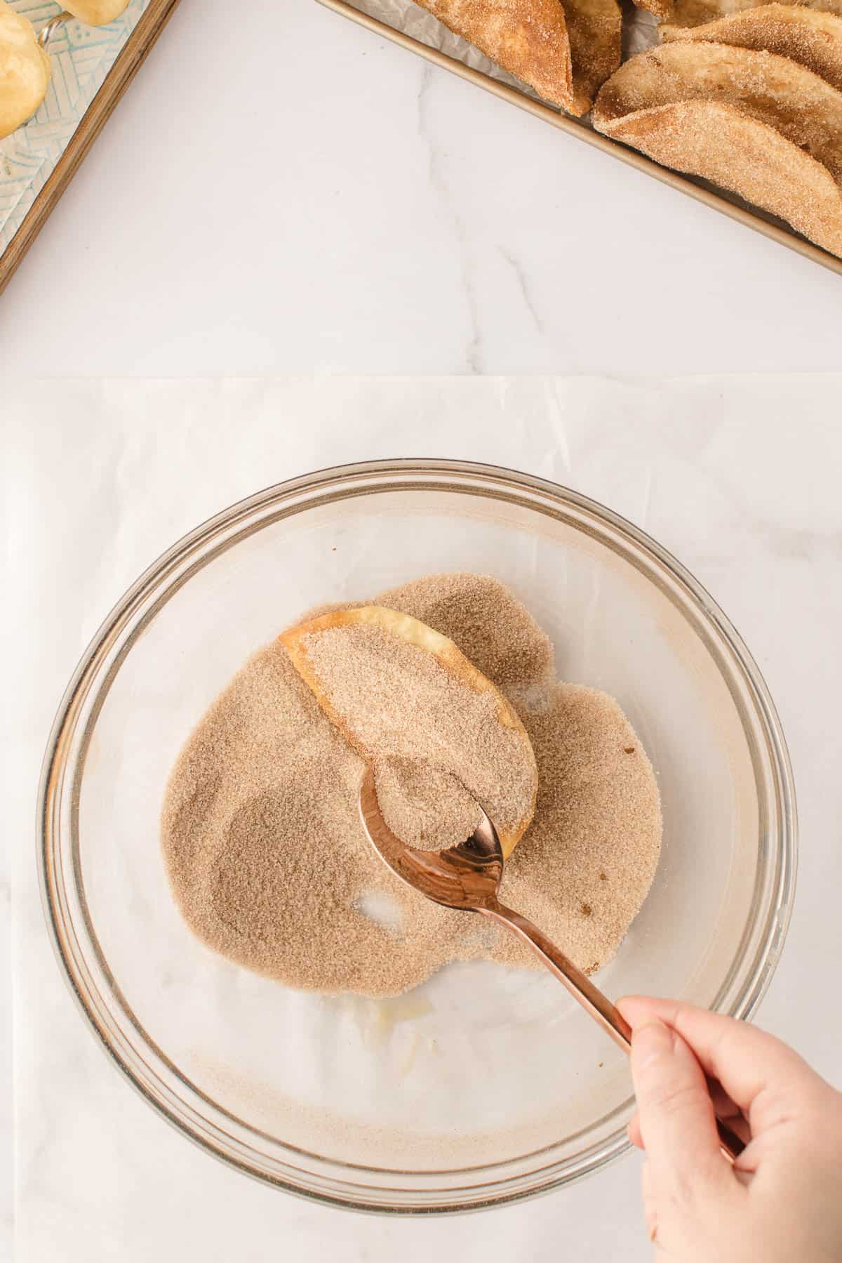 Coating fried tortilla shells with a cinnamon sugar mixture.