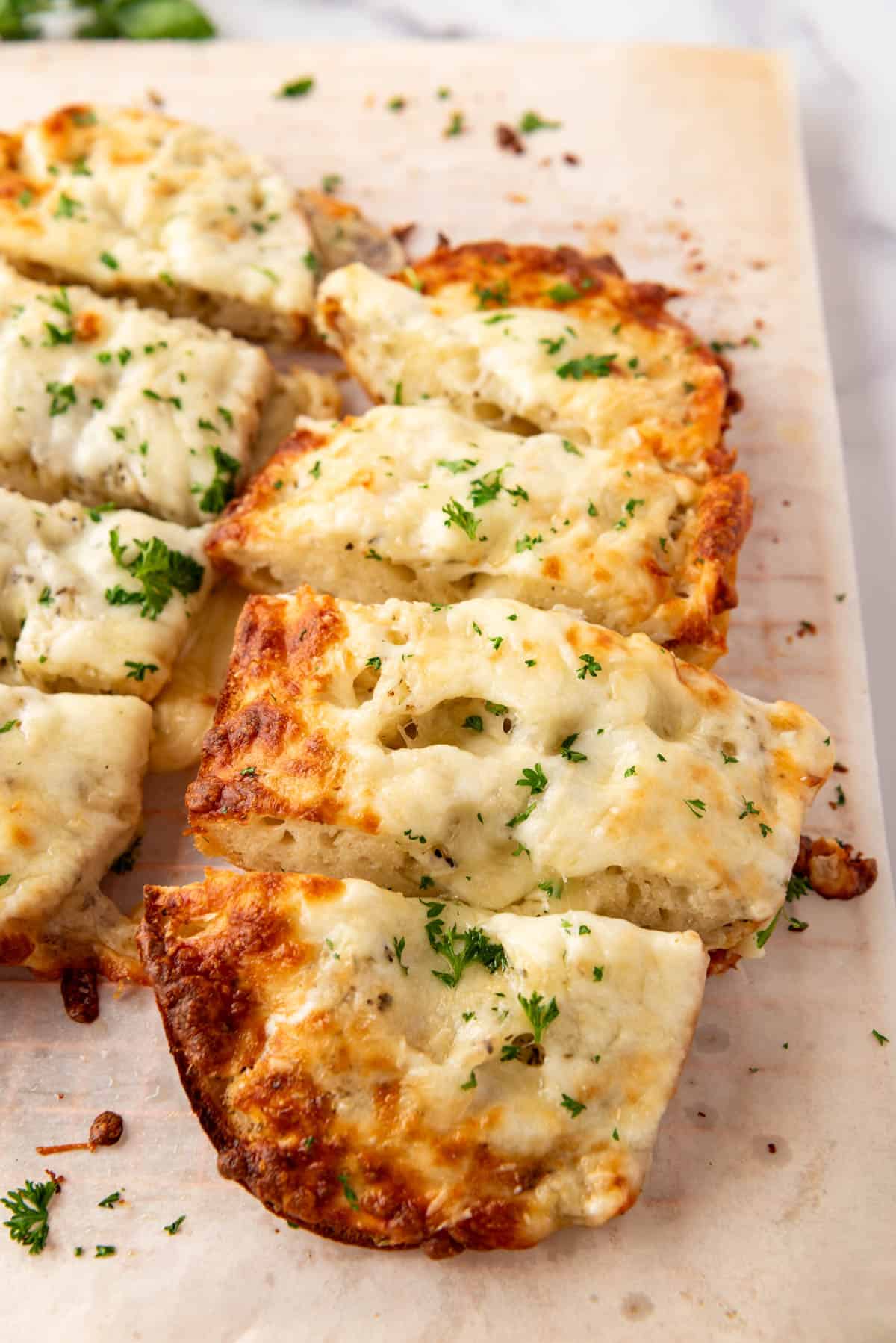 Slices of garlic bread with melted mozzarella cheese sprinkled with chopped parsley.