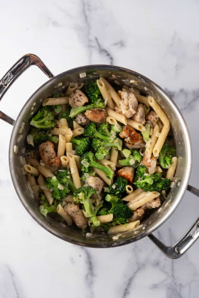 Stirring pasta, broccoli, and chicken in a large pot with creamy garlic sauce to coat before serving.