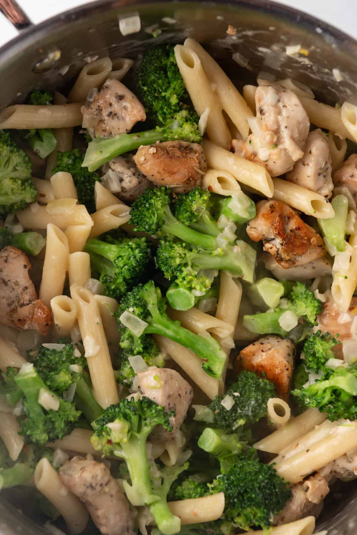 A close up image of chicken broccoli pasta in a large pot.