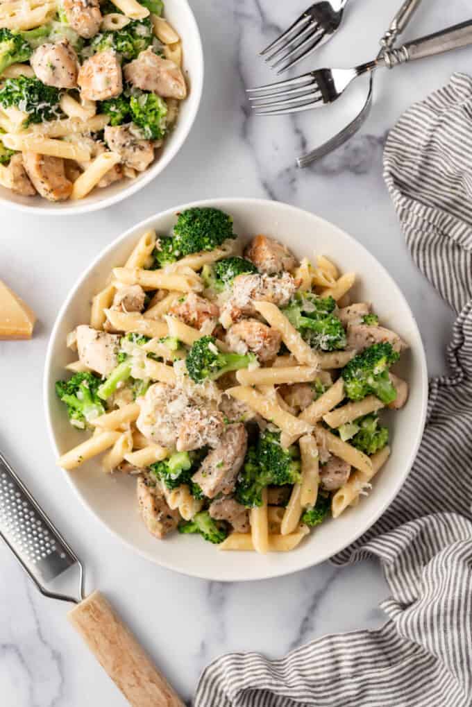 An overhead image of a bowl of chicken broccoli pasta surrounded by linen napkins and forks.