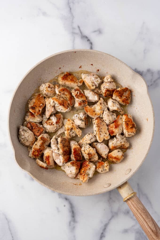 Seared chicken pieces in a large pan.