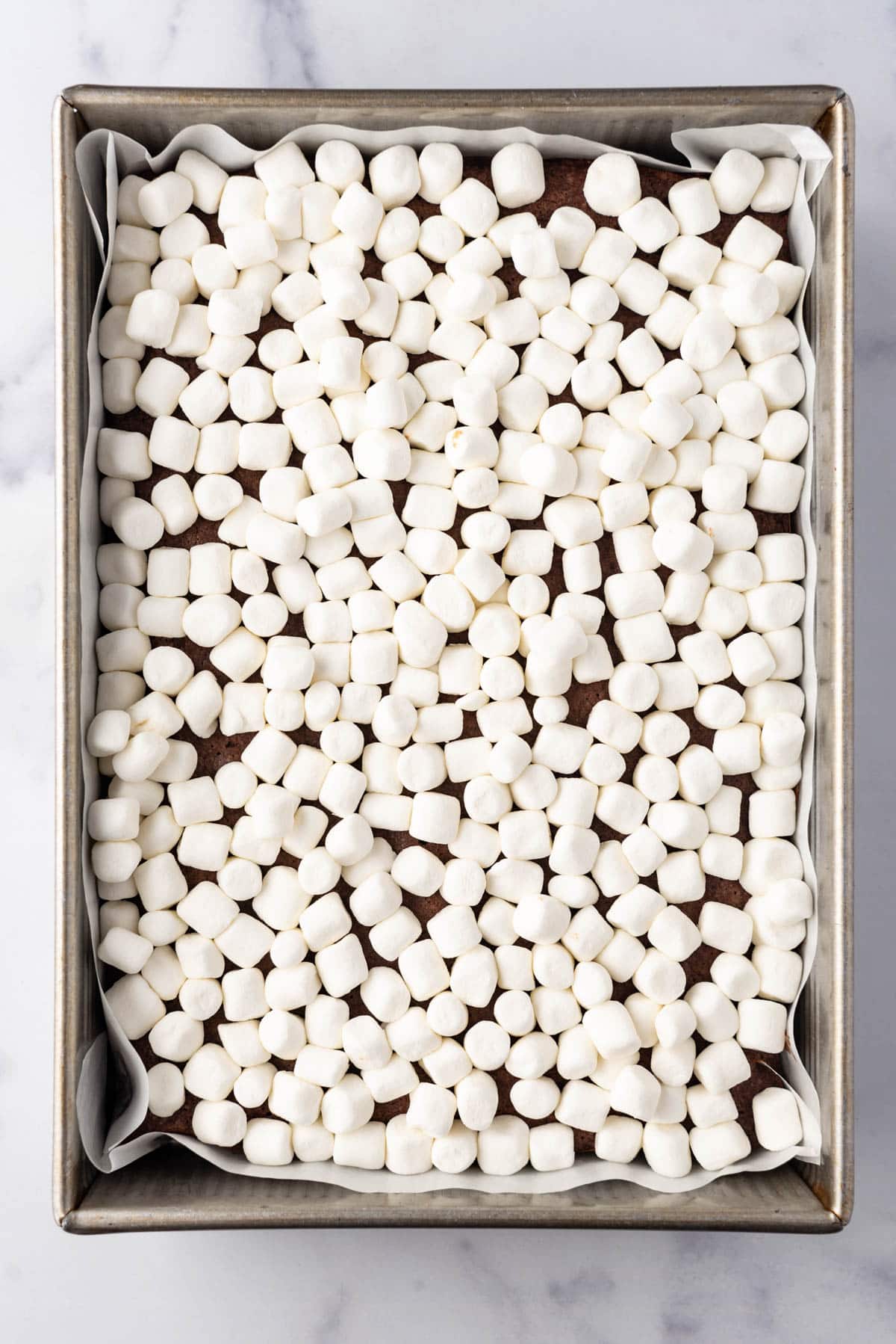 Adding a layer of miniature marshmallows to a pan of brownies.