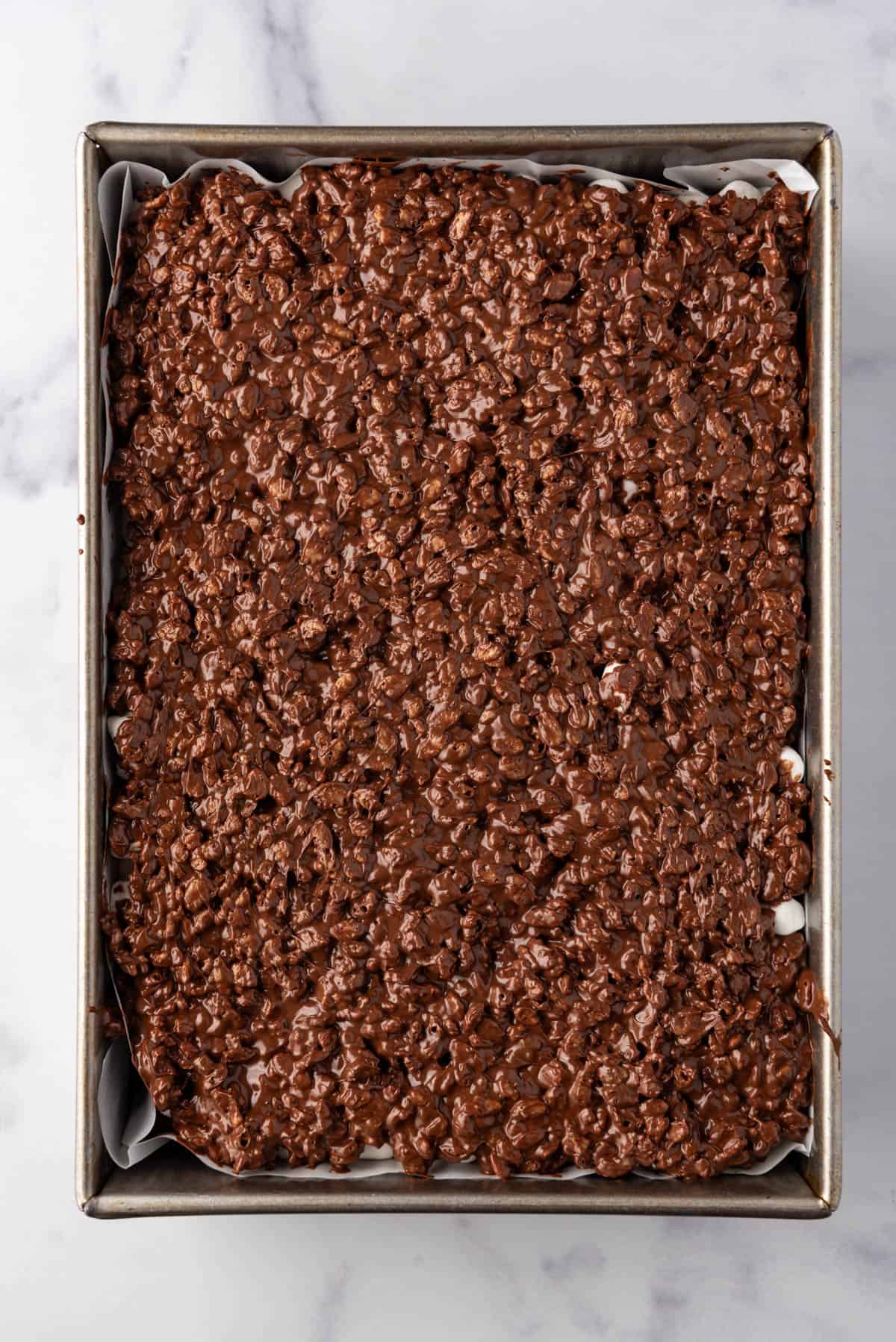 Spreading rice krispies, peanut butter, and chocolate mixture on top of brownies in a pan.