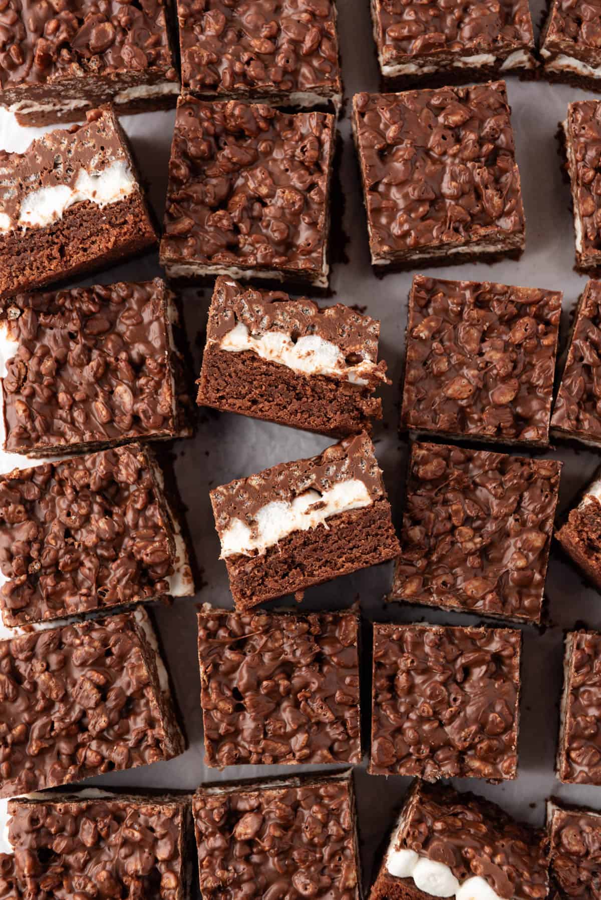 An overhead image of chocolate brownies with marshmallows and a chocolate peanut butter rice krispie topping cut into squares with some on their sides.