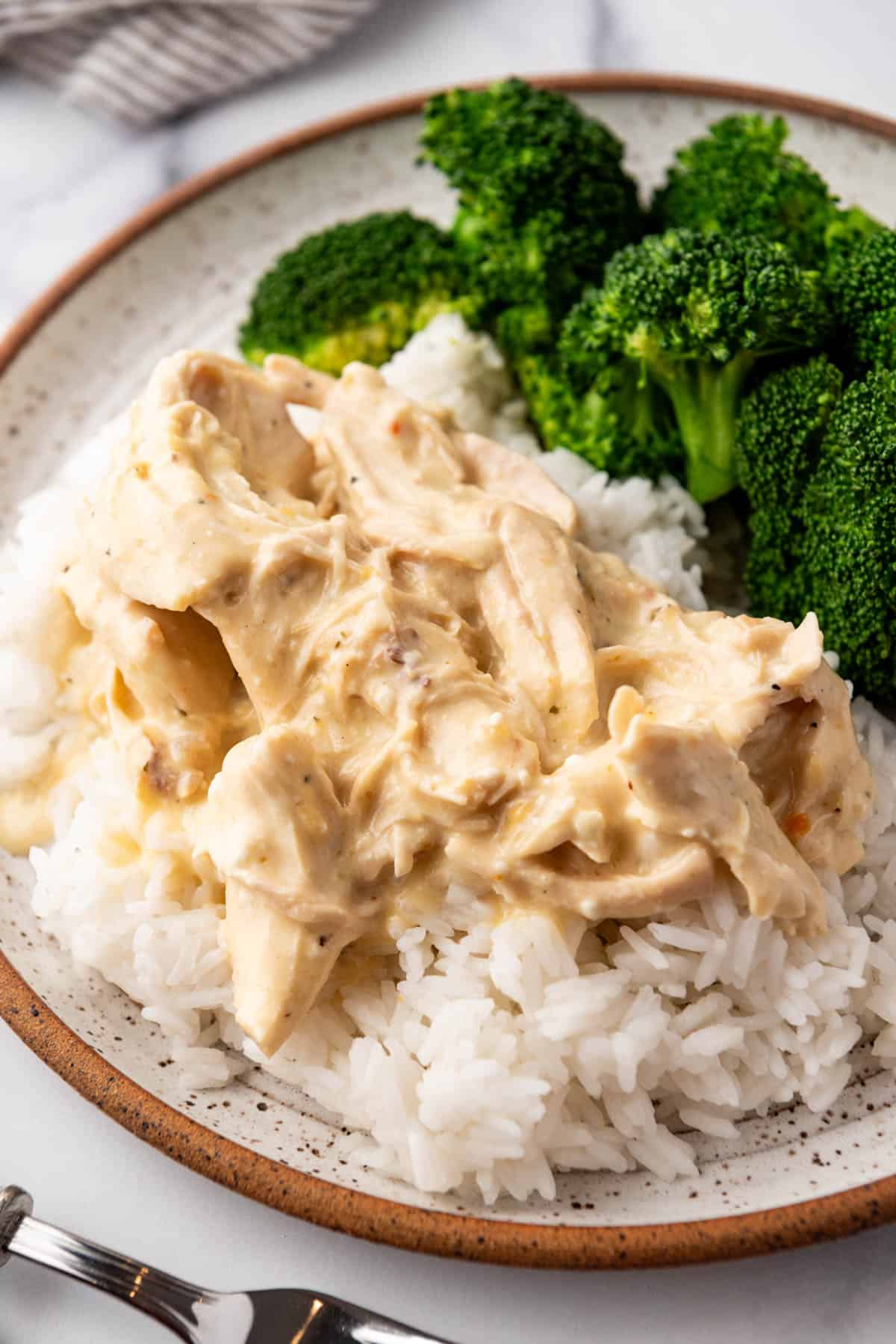 A plate of creamy crockpot Italian chicken with rice and broccoli.