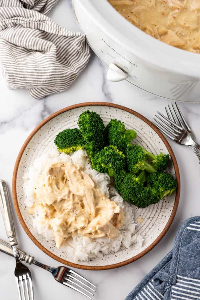 An overhead image of a plate of rice covered with creamy Italian chicken made in the slow cooker with broccoli on the side.