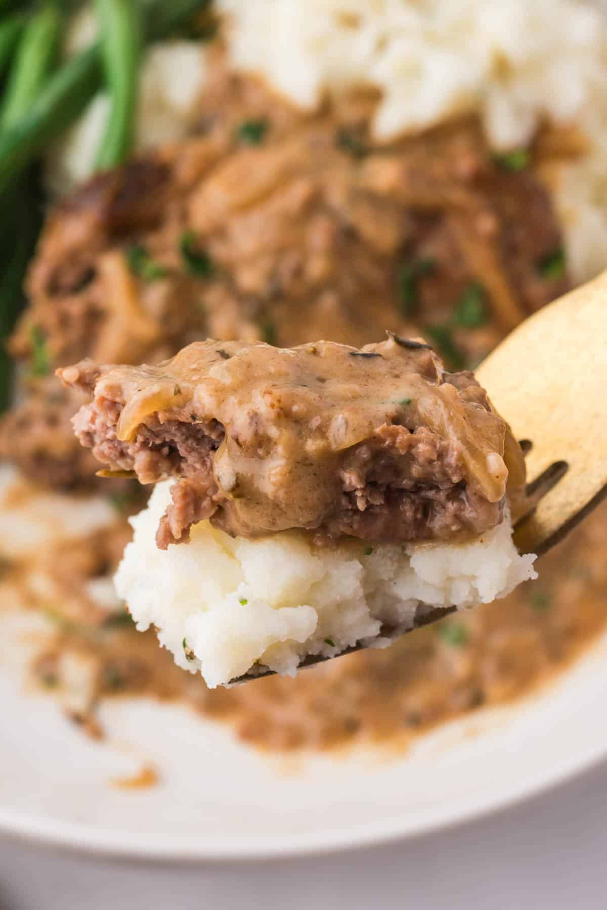 A fork holding a bite of mashed potato and slow cooker cube steak.