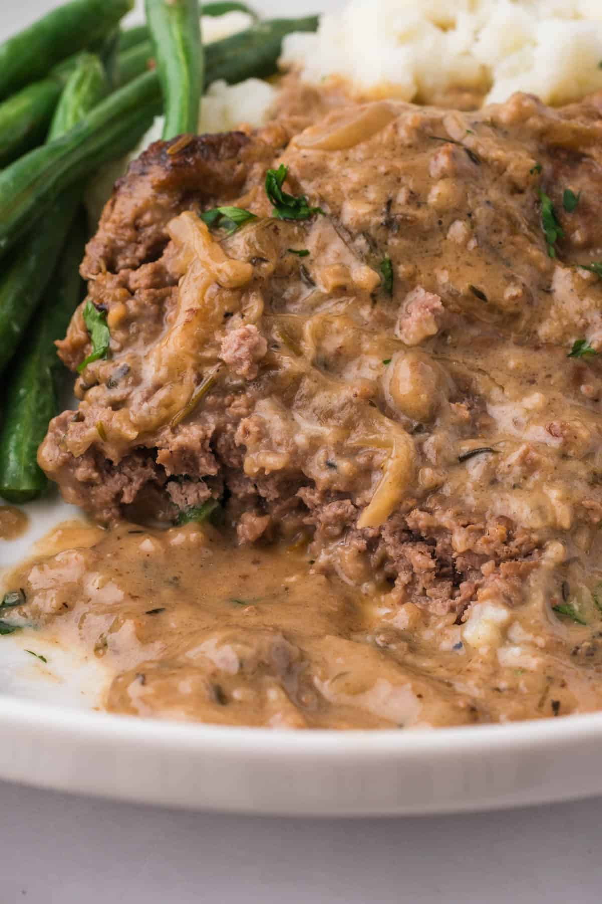 A close image of a tender cube steak with onion gravy on a plate.
