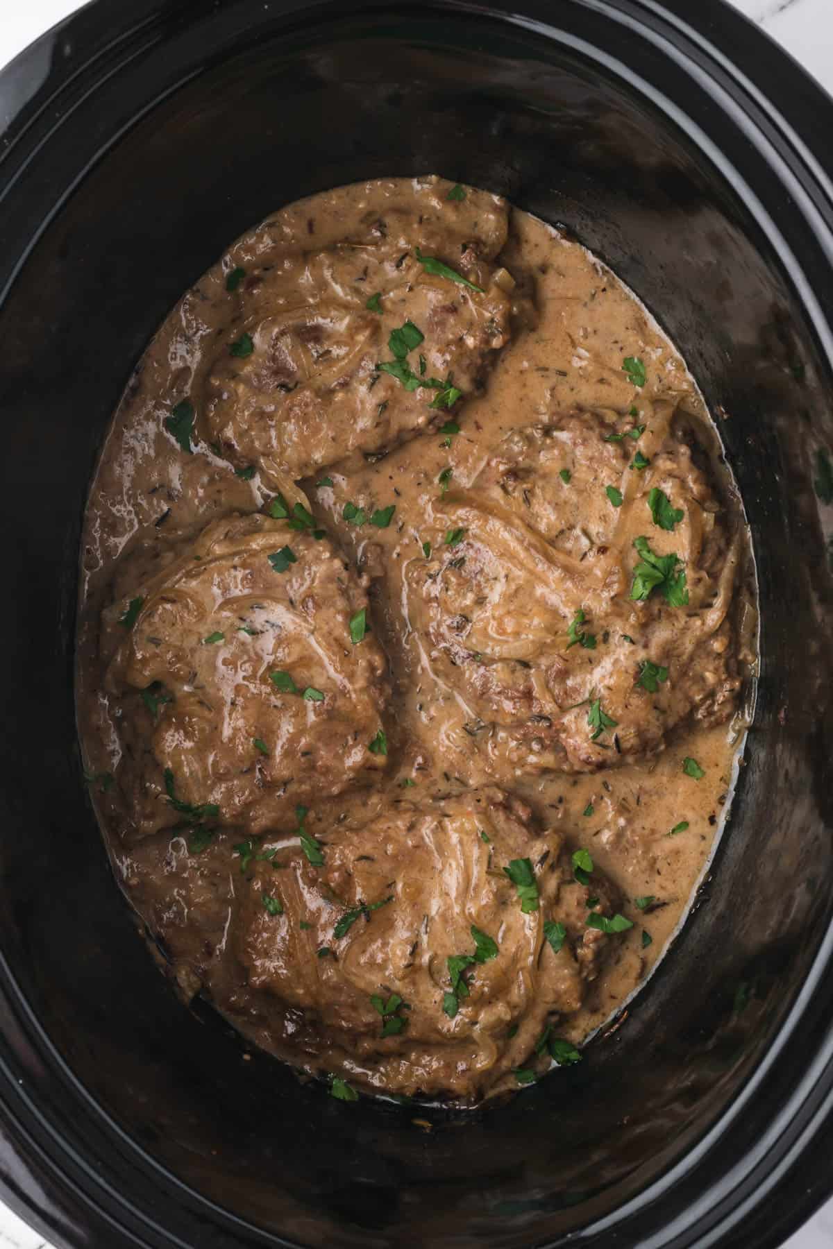 Four slow cooker cube steaks in a crock pot with sauce.