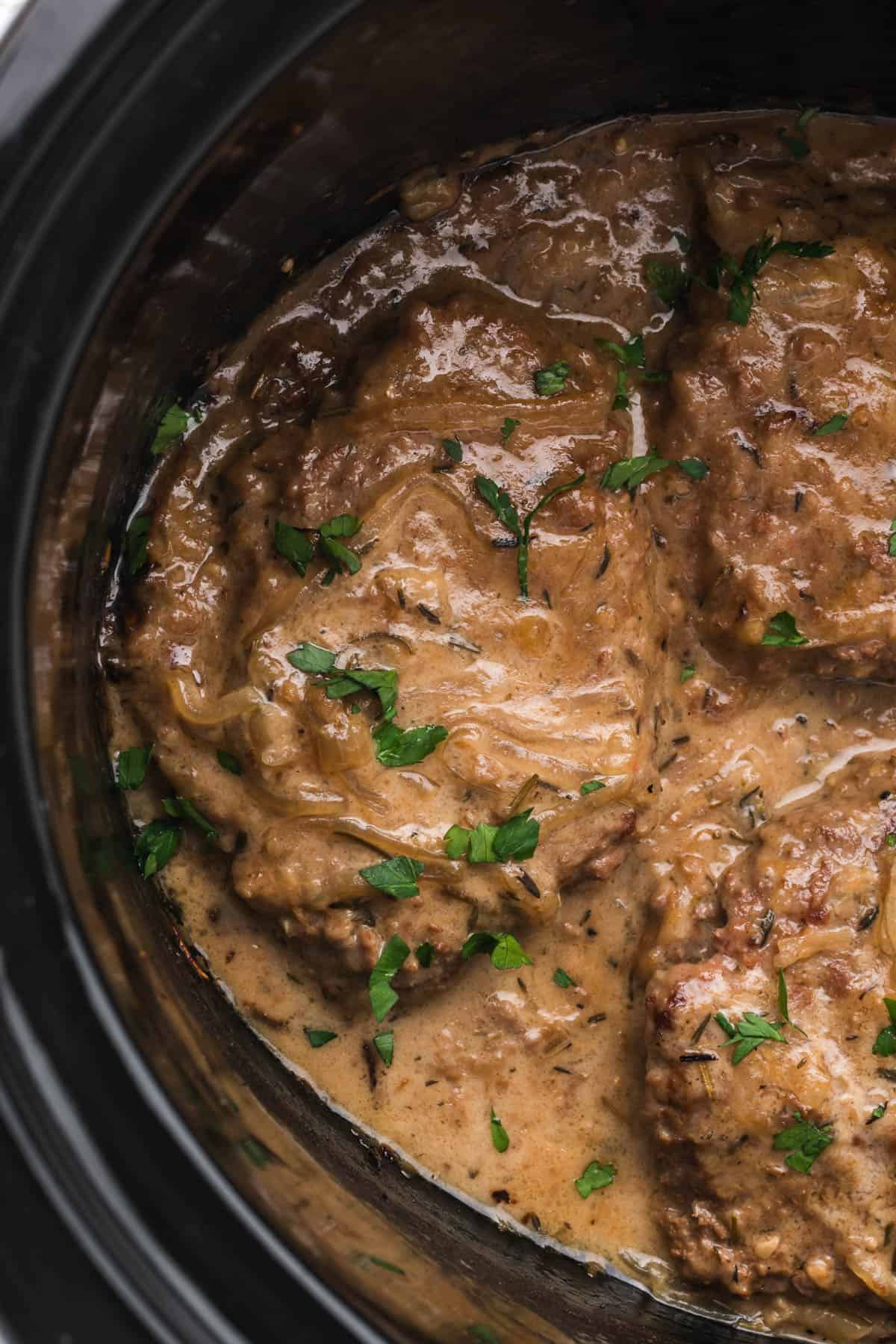 An overhead image of crock pot cubed steak with gravy in a slow cooker.