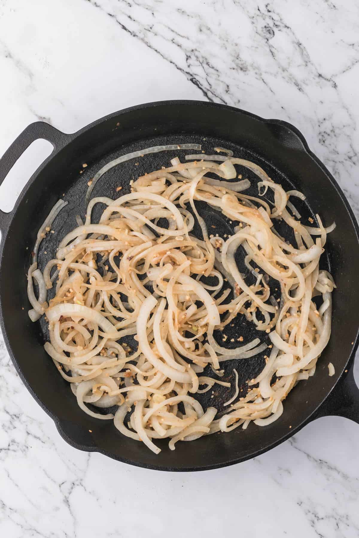 Softening sliced onions in a large cast iron skillet.