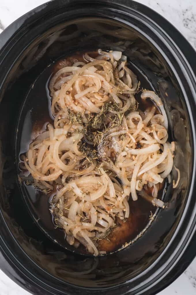 Softened onions piled on top of cube steaks in a slow cooker.