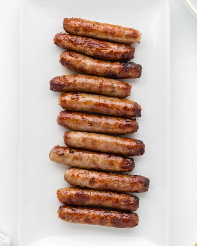 An overhead image of sausage links that have been cooked in the air fryer on a white plate.