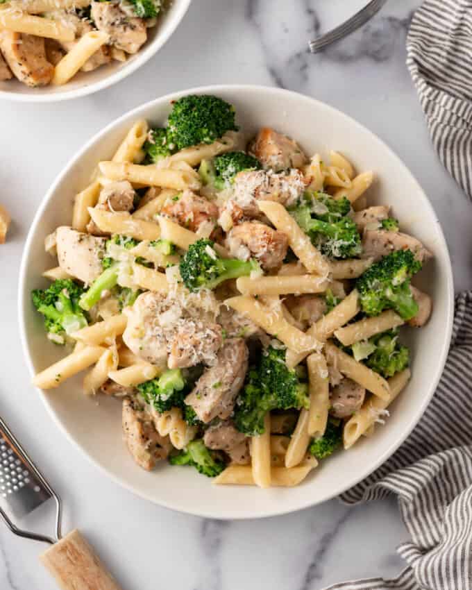 An overhead image of a bowl of chicken broccoli pasta surrounded by linen napkins and forks.
