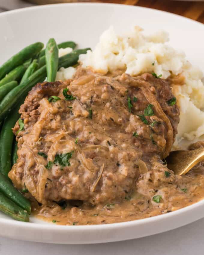 A plate of cube steak with gravy over mashed potatoes with green beans on the side.