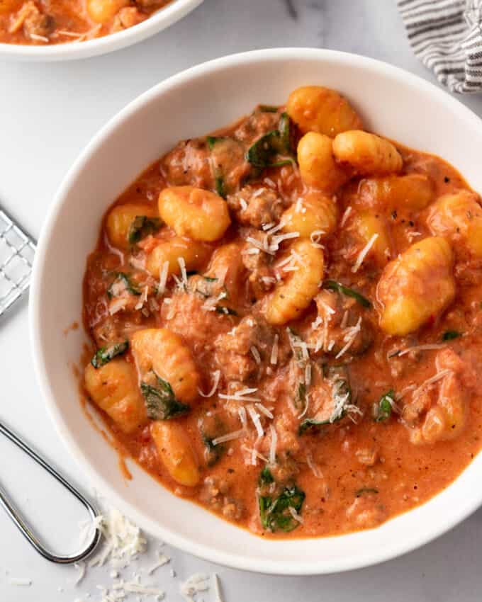 A bowl of creamy sausage gnocchi with parmesan cheese sprinkled on top.