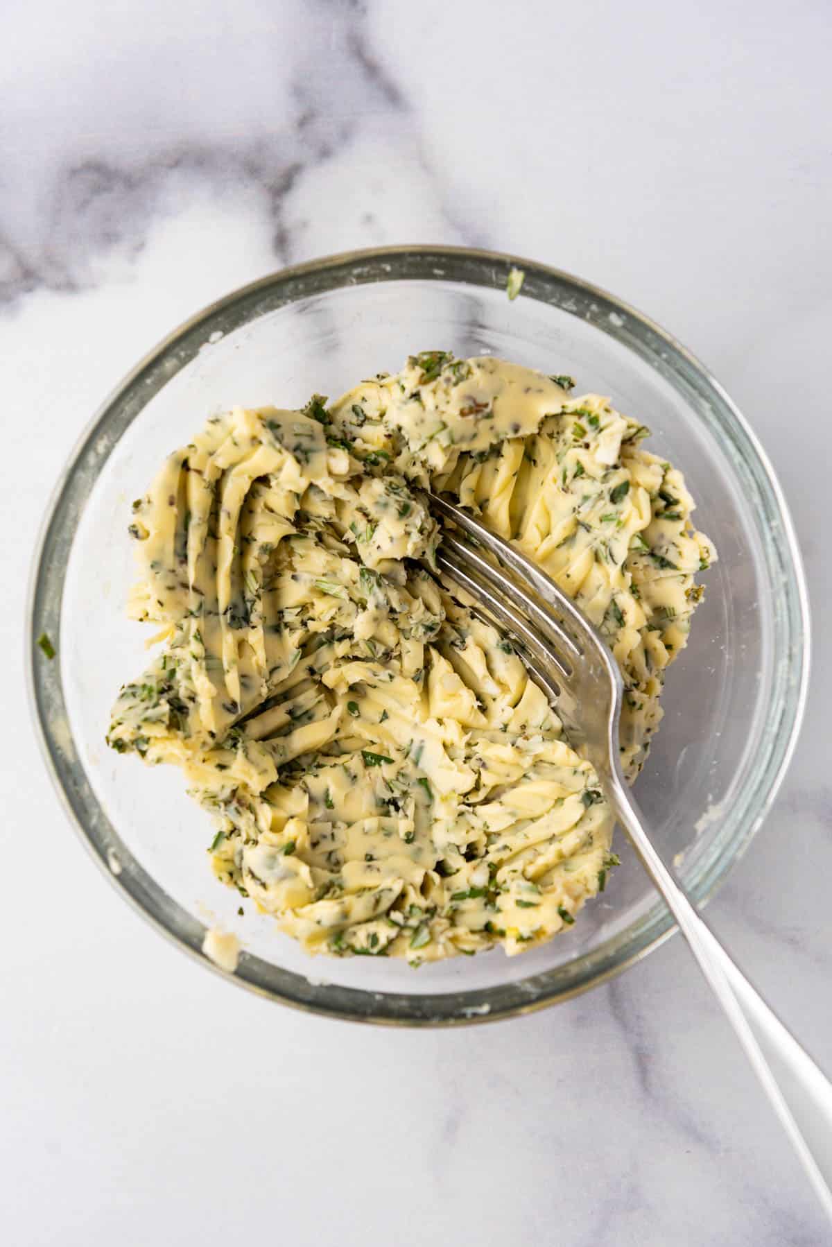 Mashed garlic  herb butter in a bowl with a fork.