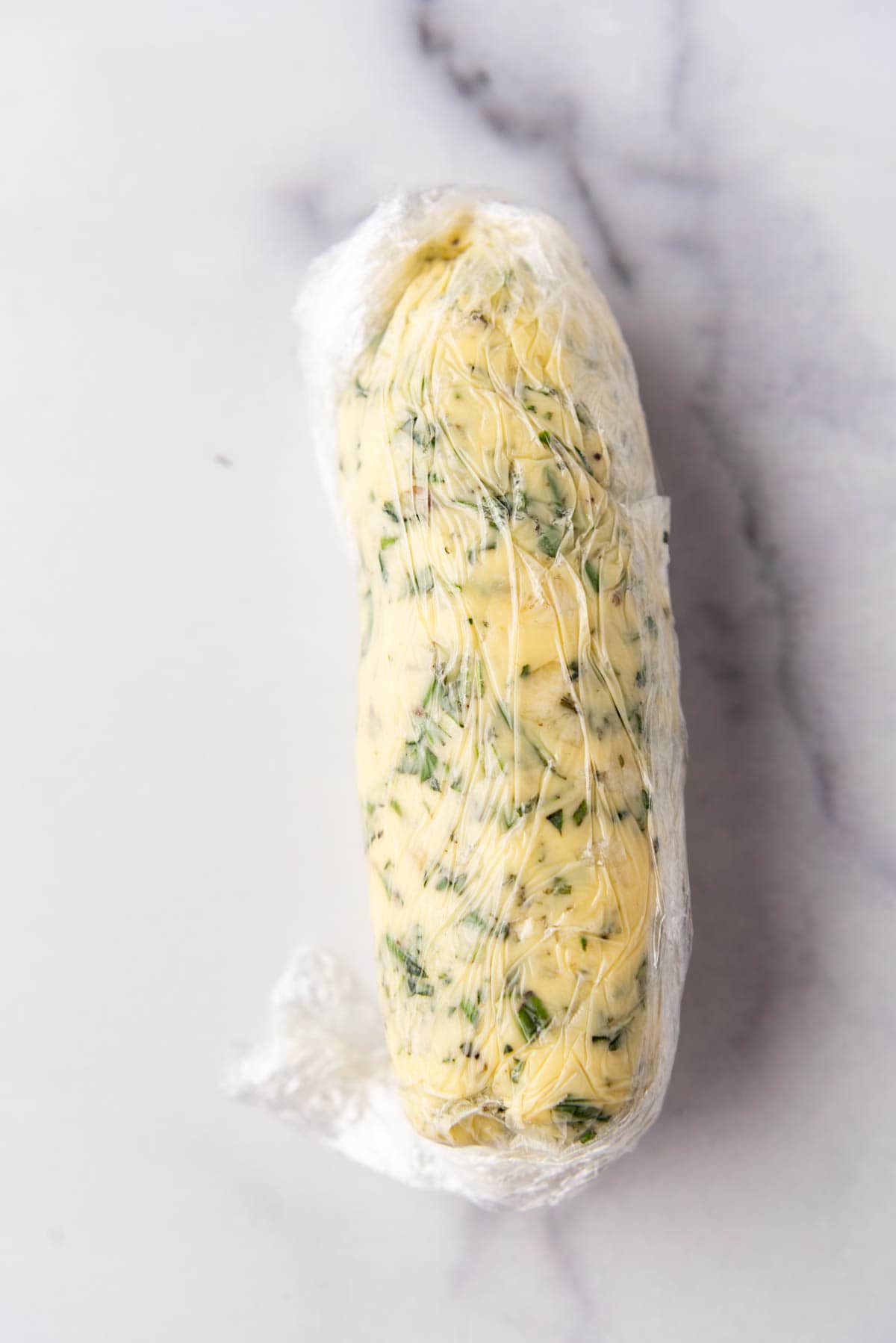 Garlic herb butter wrapped up in plastic wrap into a log shape.