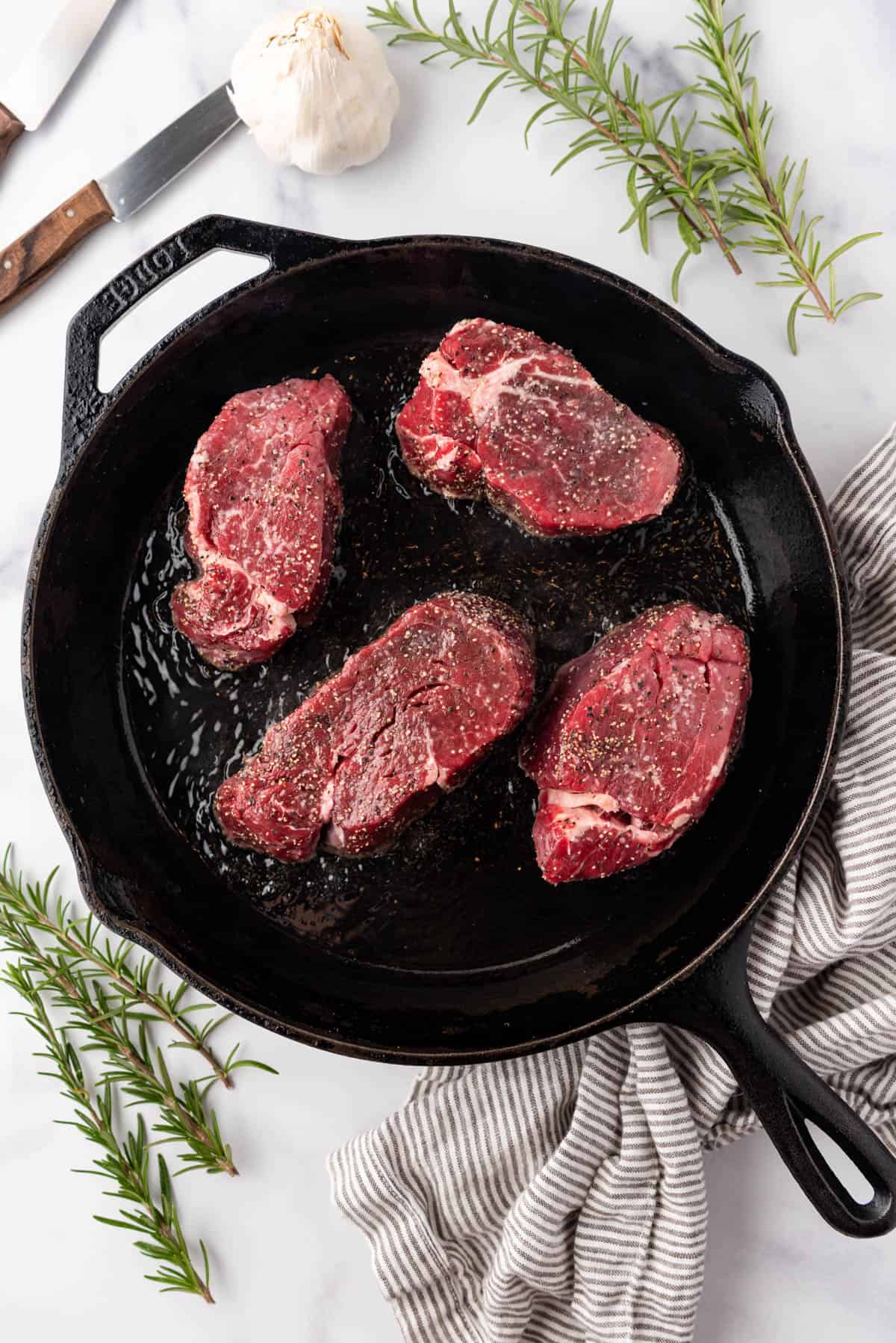 Adding seasoned filet mignon to a very hot cast iron skillet to sear it.