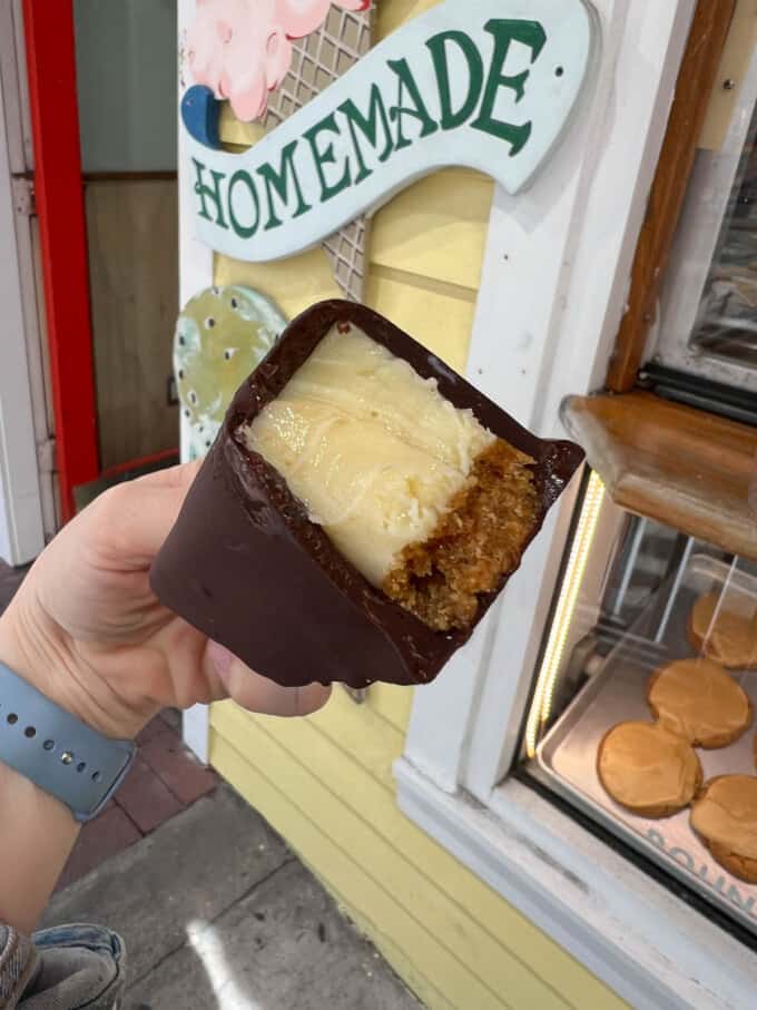 A chocolate covered key lime pie bar on a stick with a bite taken out of it.