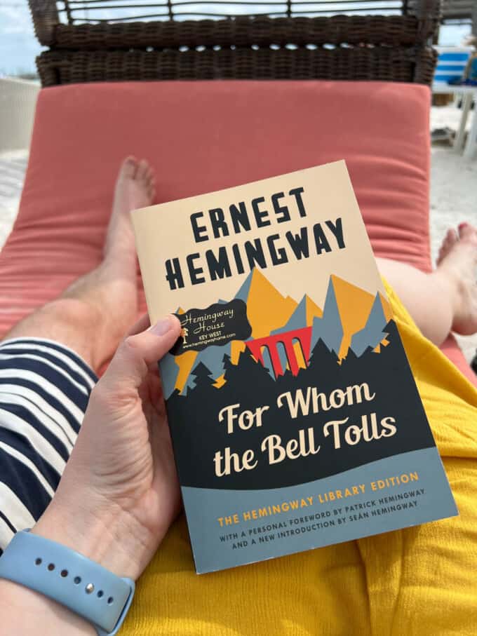 A hand holding "For Whom The Bell Tolls" by Ernest Hemingway.