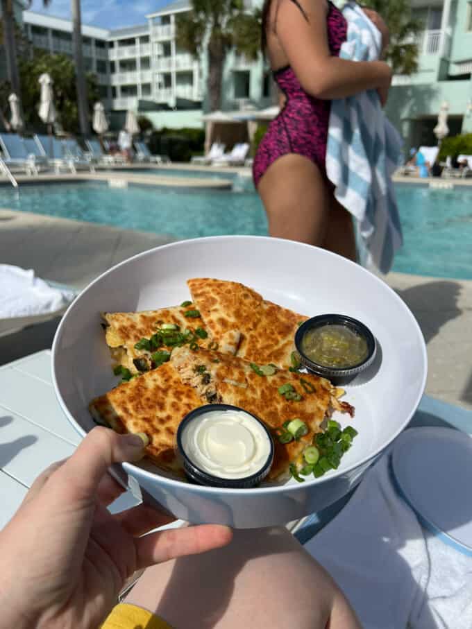 An image of a hand holding a plate of chicken quesadillas in front of a pool in the Florida Keys.
