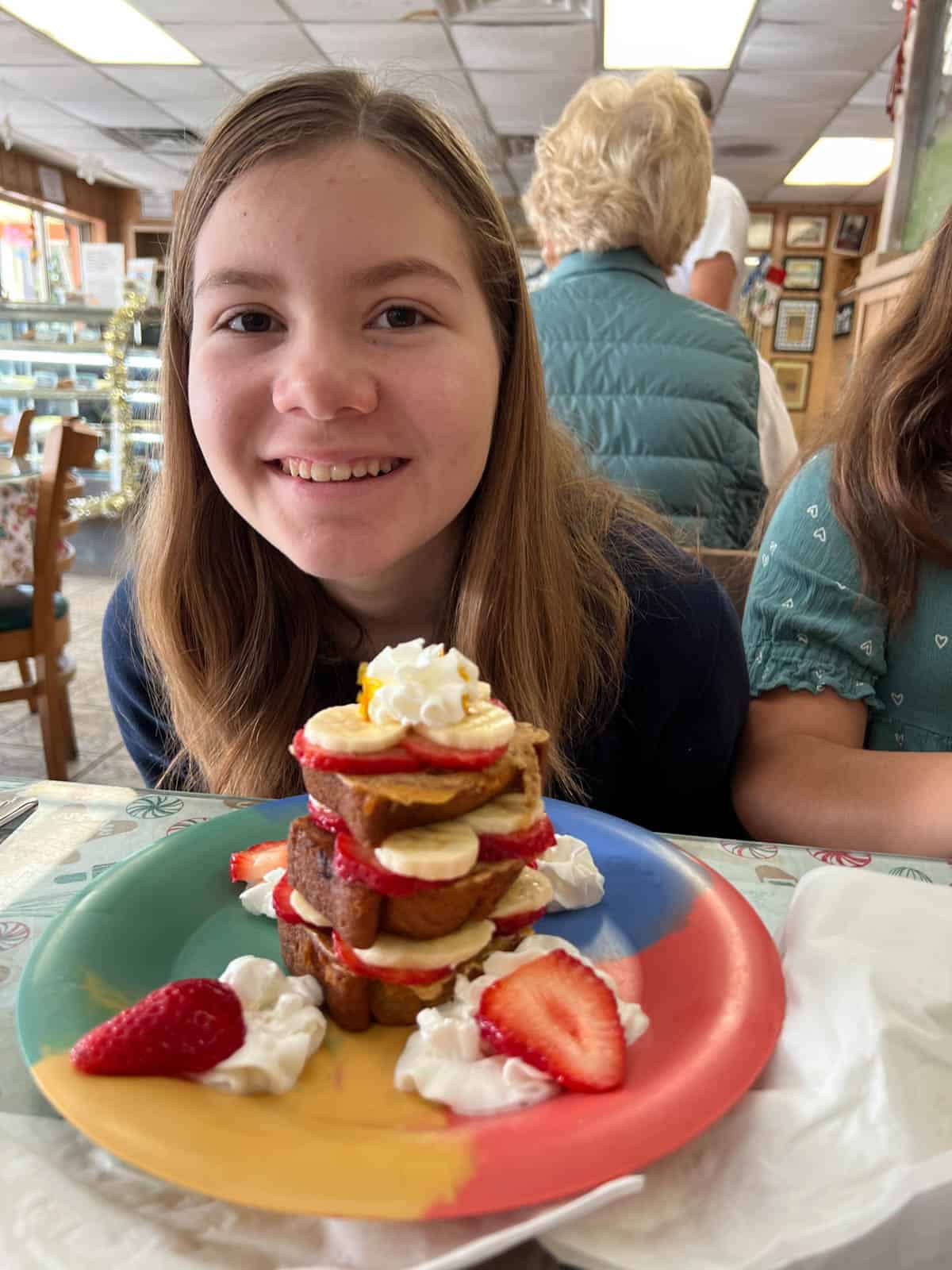 A girl with a stack of banana bread french toast with fresh fruit.