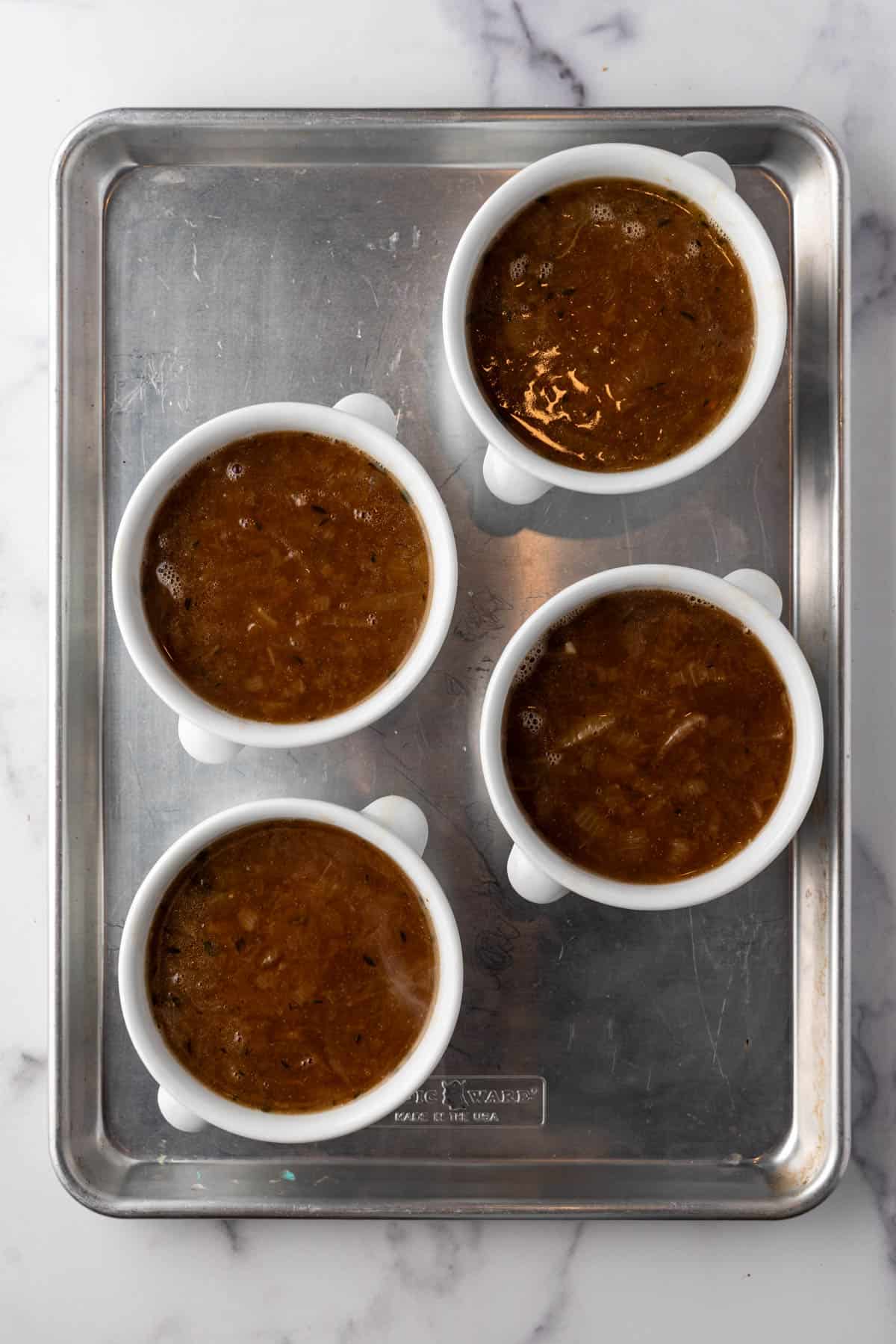 Four white bowls filled with homemade French onion soup on a baking sheet.