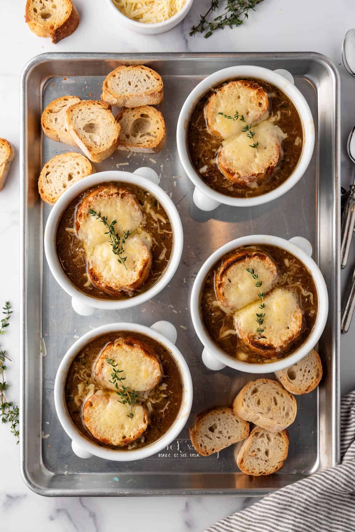Finished French onion soup in separate bowls on a baking sheet.