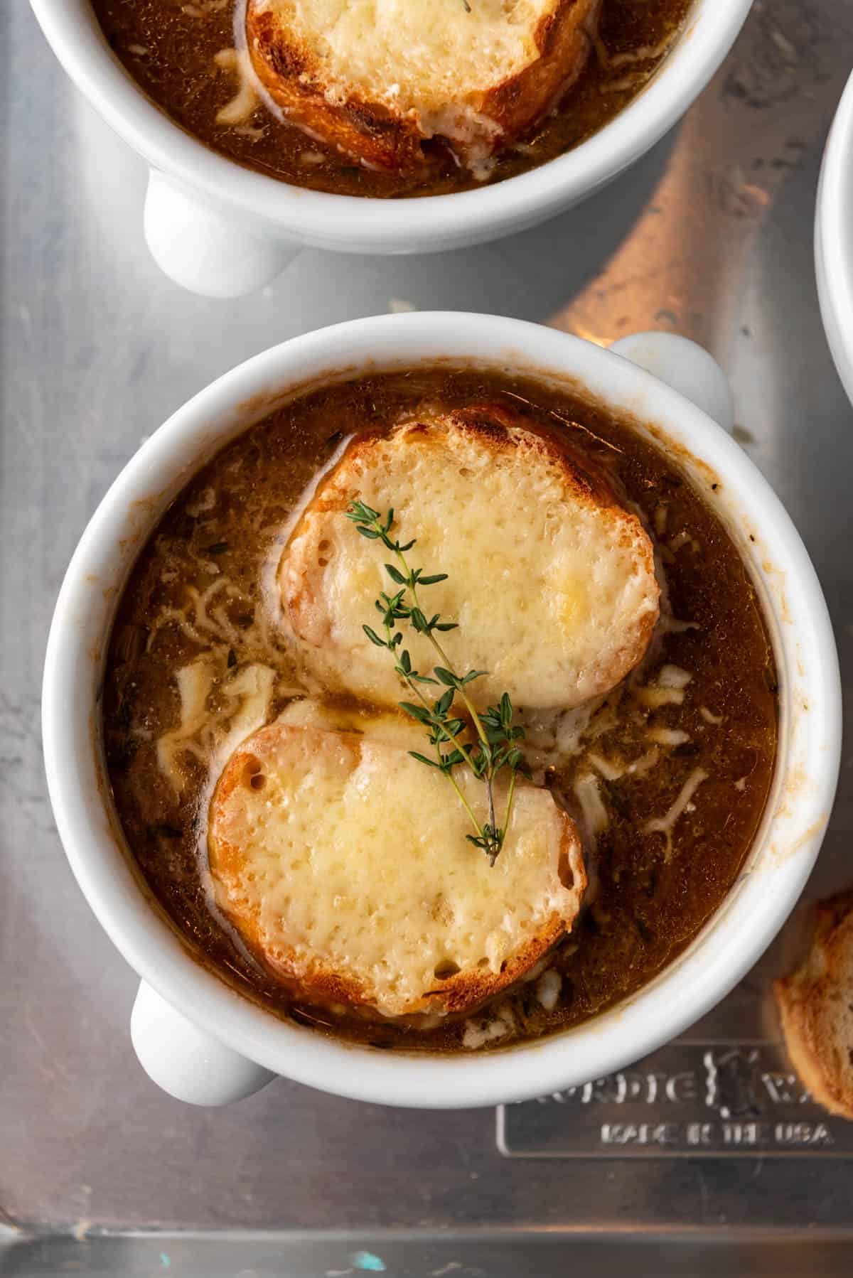 A bowl of French onion soup with baguette slices and melted gruyere cheese on top.