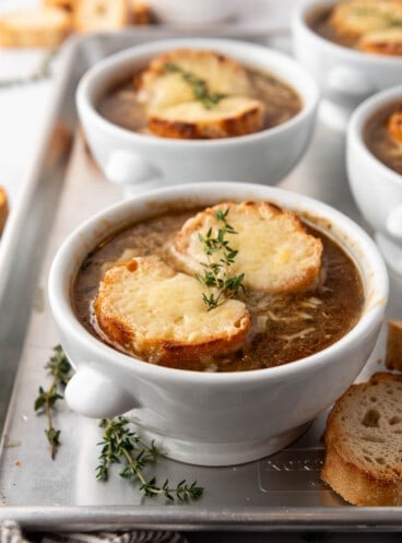 Bowls of French onion soup with melted bread and baguette slices on top.