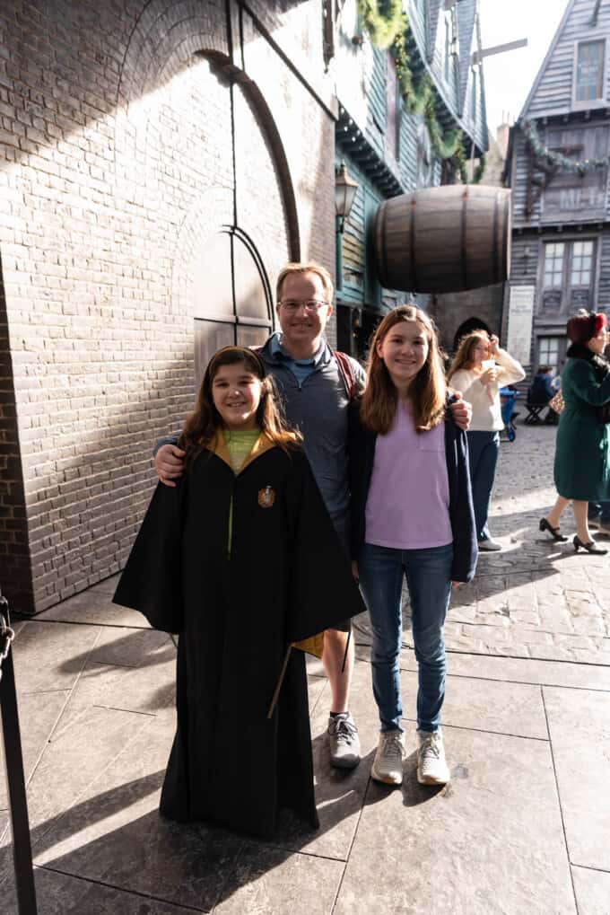 An image of a dad and two daughters with one in wizarding robes.