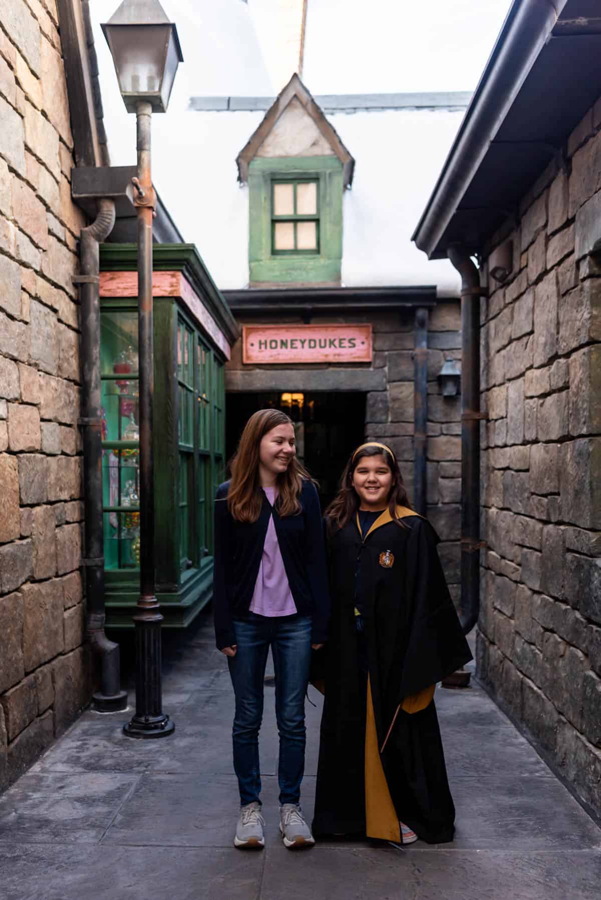 An image of two girls outside of Honeyduke's in Hogsmeade with one of them in wizard robes.