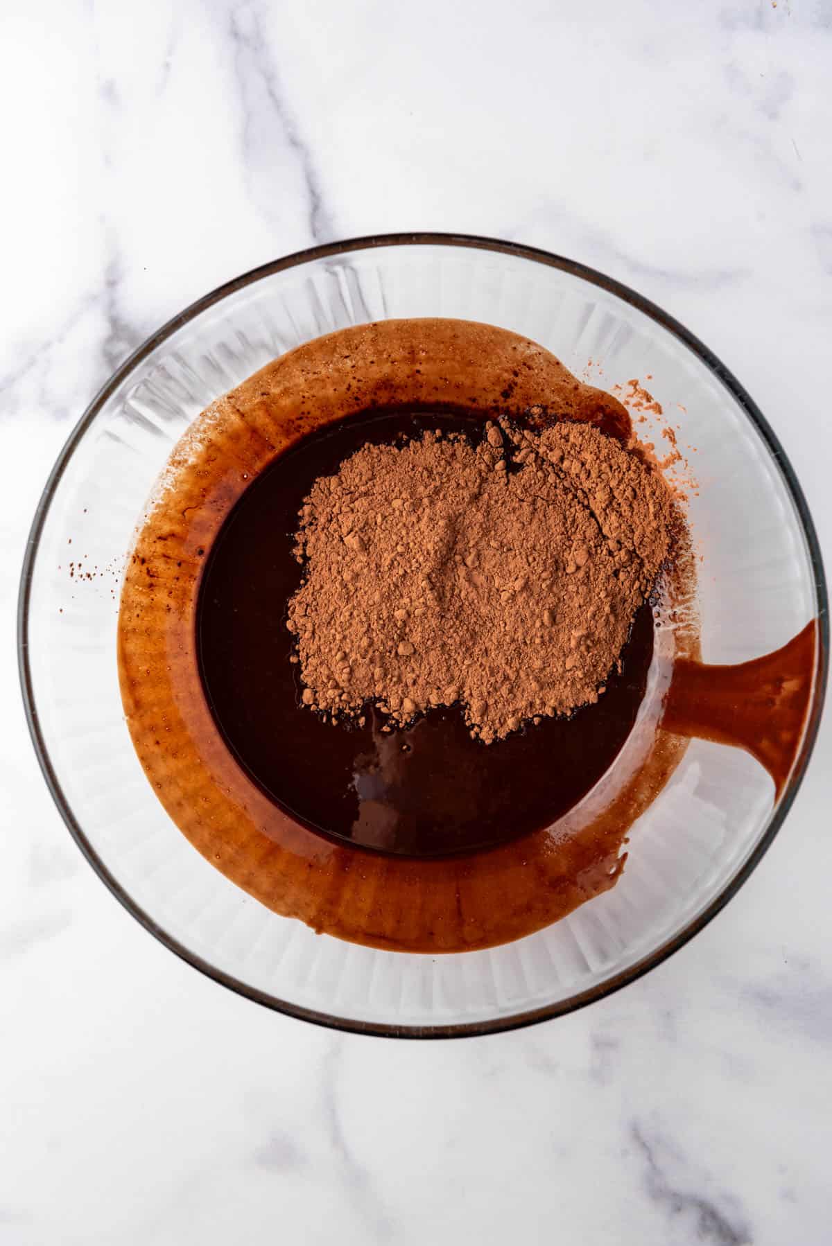 Adding cocoa powder to melted chocolate and butter in a bowl.