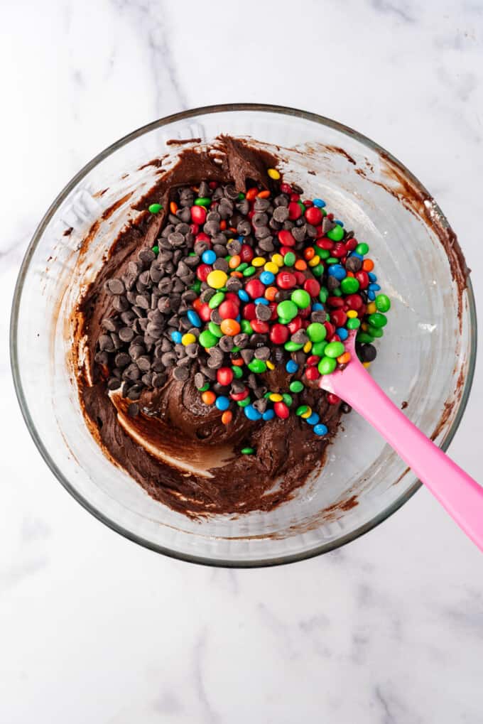 Adding chocolate chips and rainbow M&M's to brownie batter.