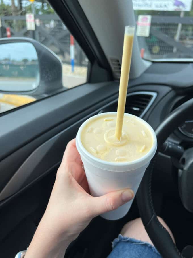 A mango-passionfruit-banana milkshake in a styrofoam cup with a straw.