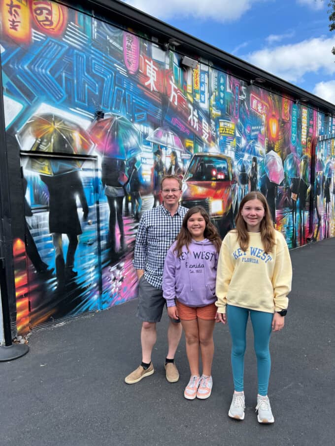 A dad and two daughters in front of a graffitied mural at Wynwood Walls in Miami.