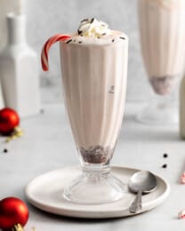 An image of a tall milkshake glass filled with peppermint bark milkshake and a candy cane.