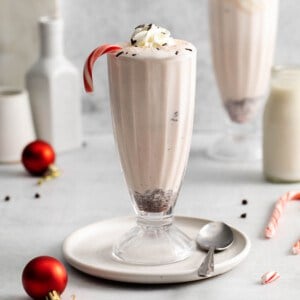 An image of a tall milkshake glass filled with peppermint bark milkshake and a candy cane.