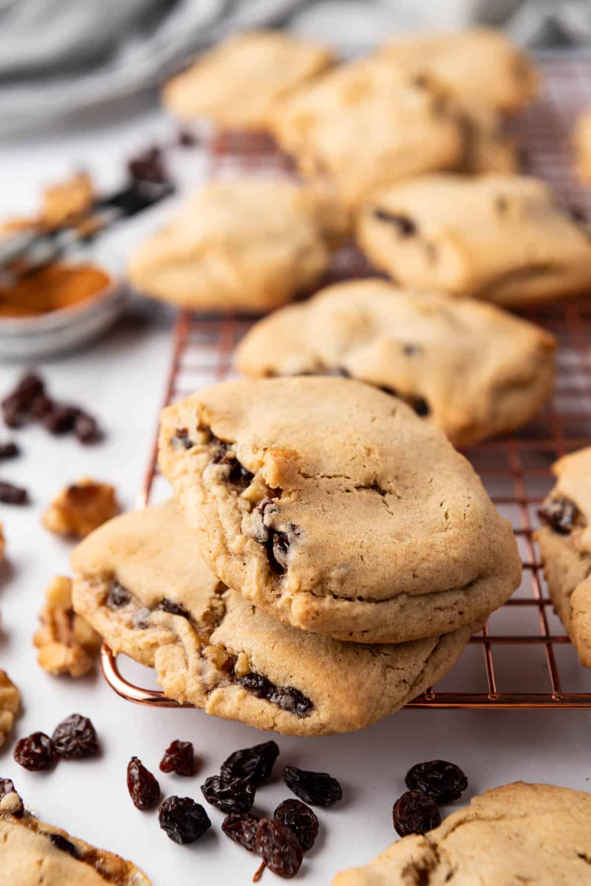 An image of two stacked raisin-filled cookies with raisins and walnuts and more cookies scattered around them.