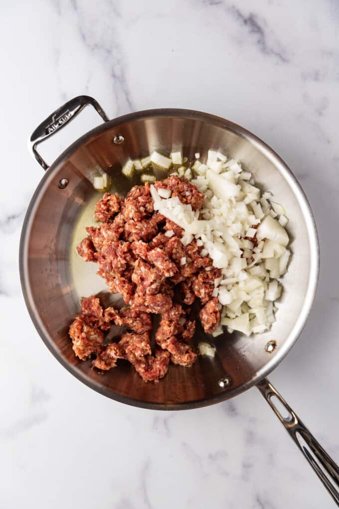 Adding crumbled Italian sausage with casings removed and chopped onions to a large skillet.