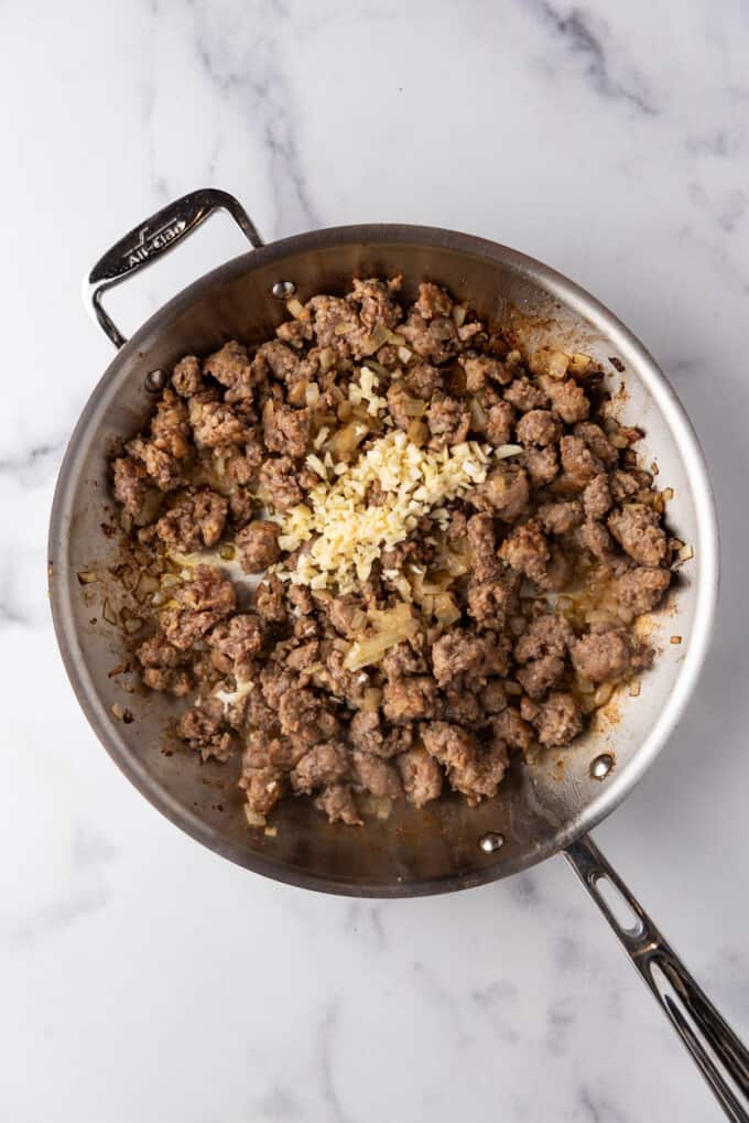 Adding minced garlic to browned Italian sausage and onions in a large skillet.