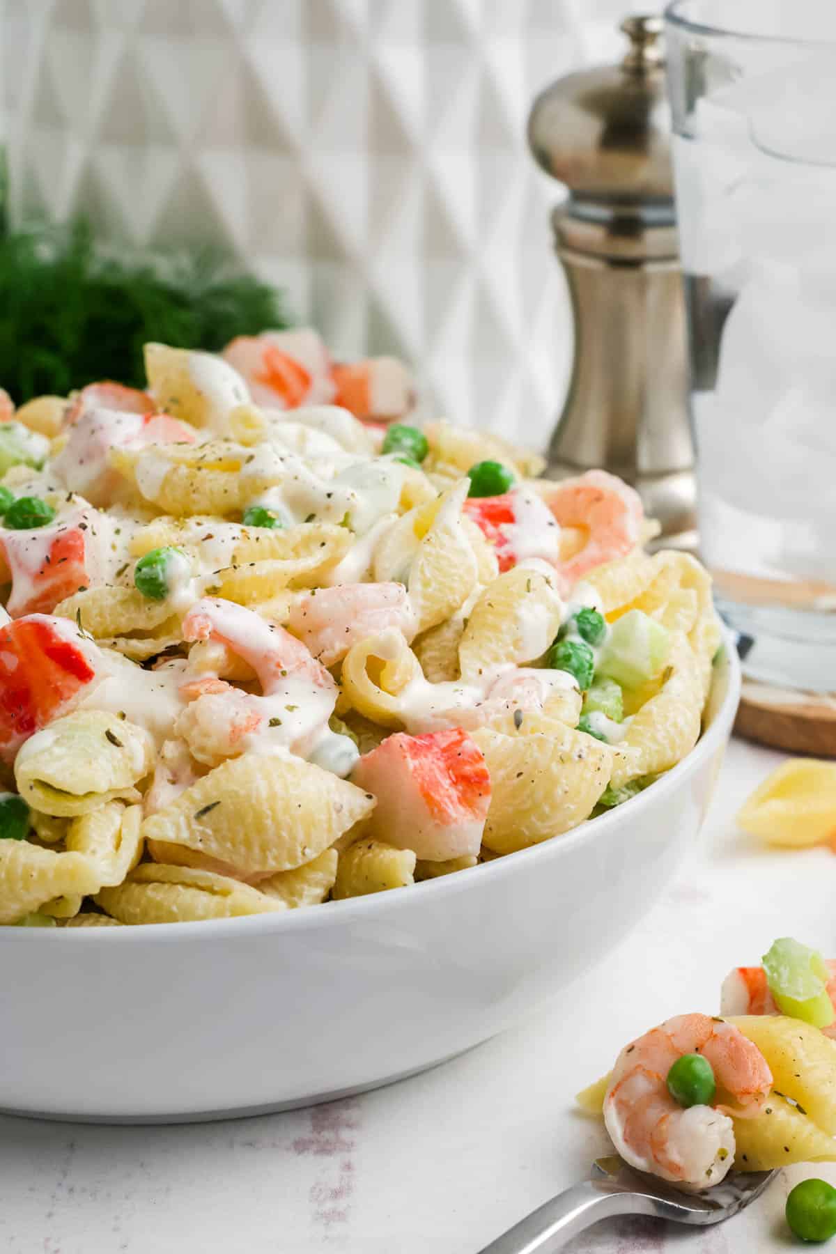 A side view of a bowl of seafood pasta salad in a white serving bowl.