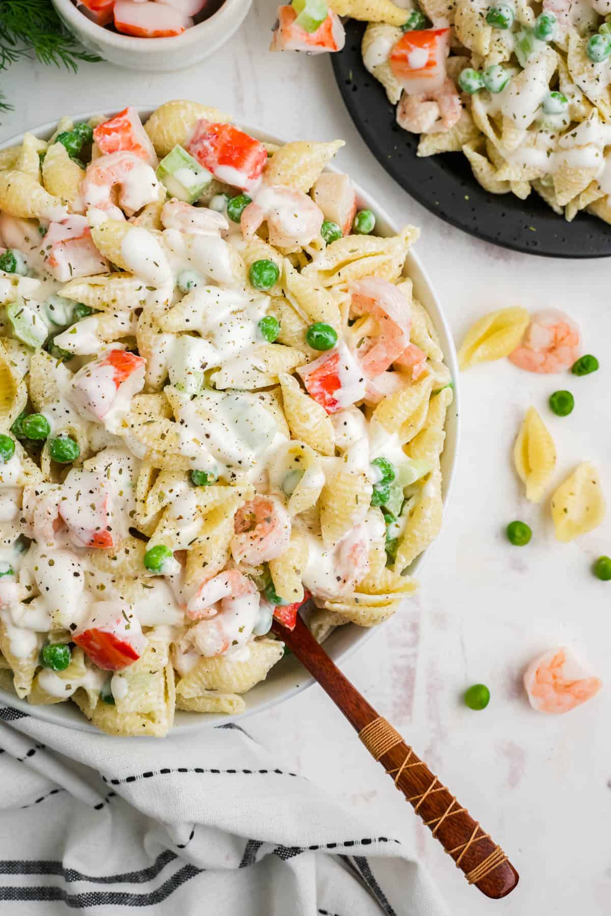 A spoon in a large serving bowl of pasta salad with shrimp.