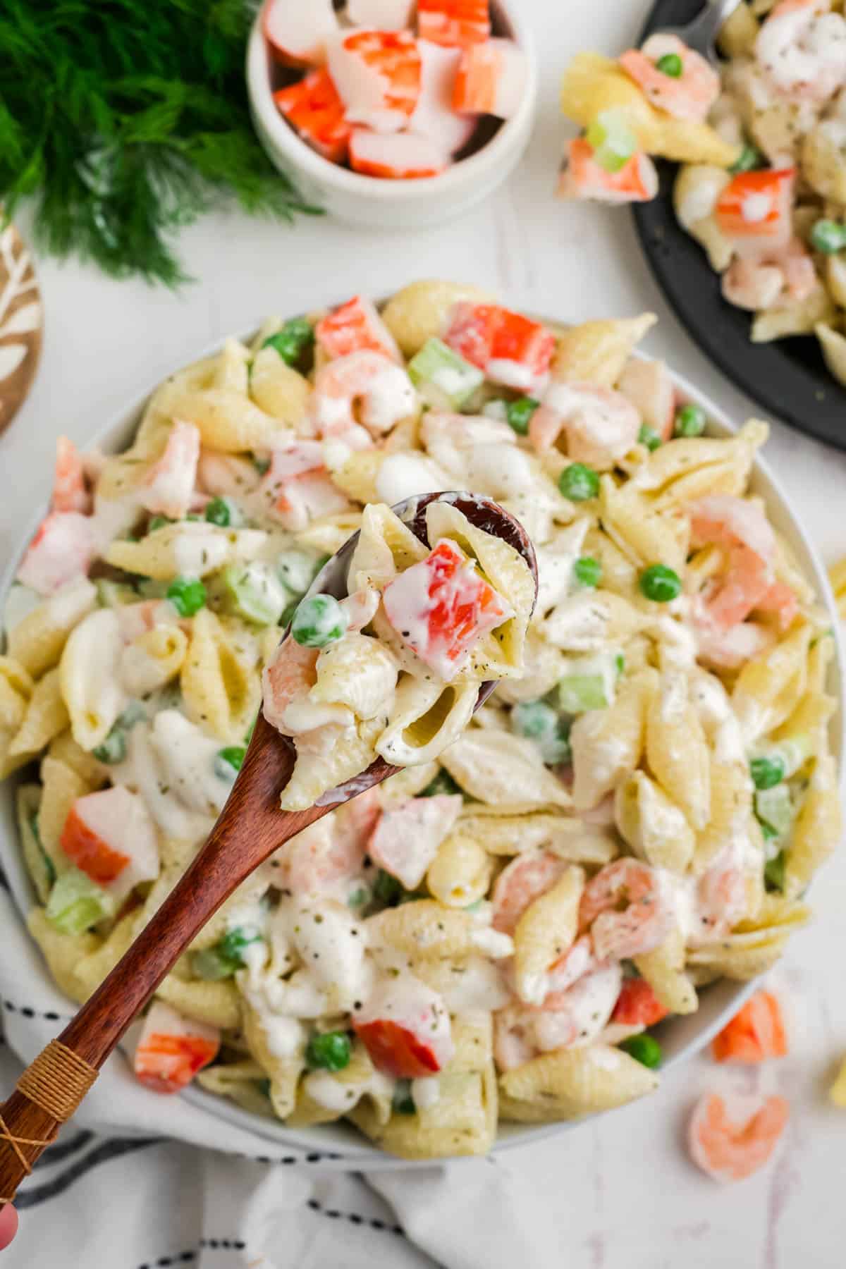 A spoon lifting up a large bite of seafood pasta salad with crab and shrimp.