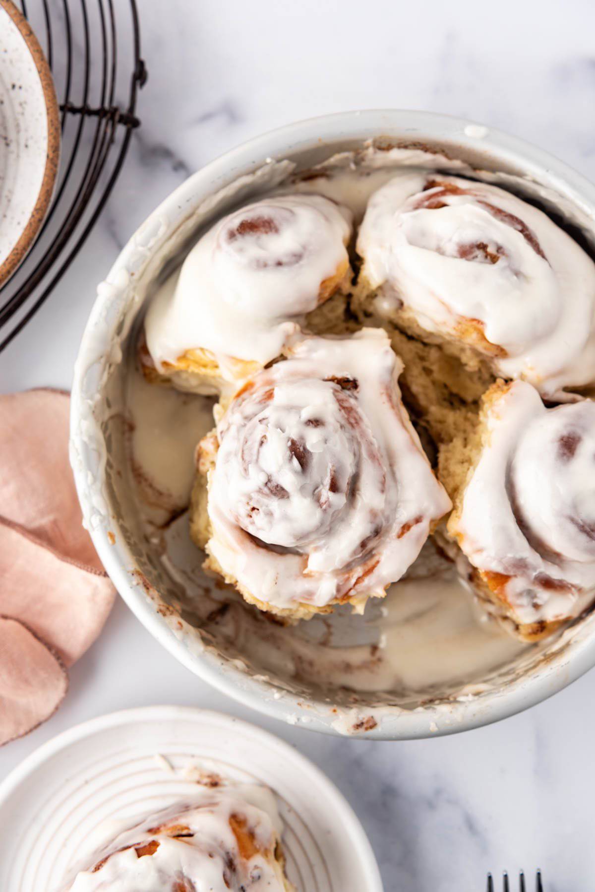 A small batch of cinnamon rolls with a couple removed from the pan.